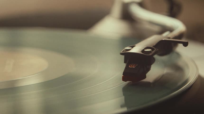 A close-up shot of a turntable needle playing a spinning vinyl record with a vintage aesthetic