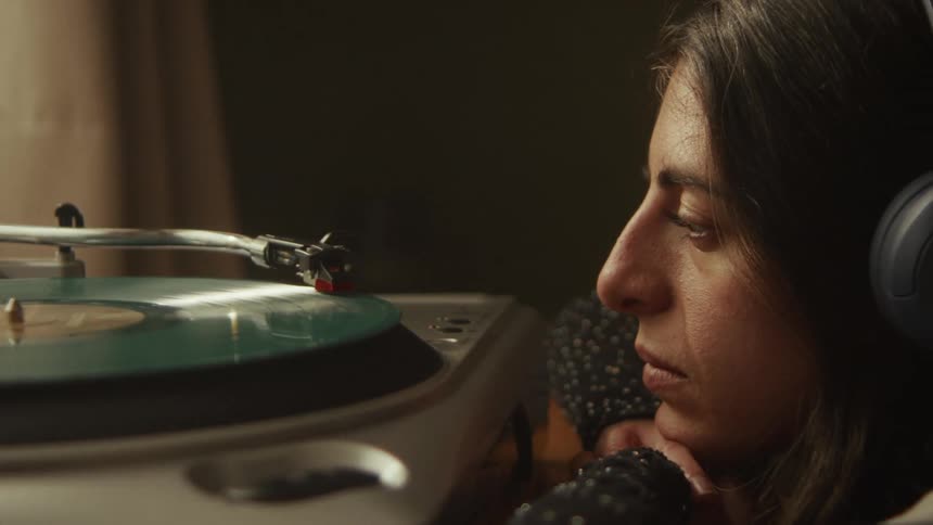 Close-up of a contemplative woman wearing headphones while listening to a spinning vinyl record on a turntable