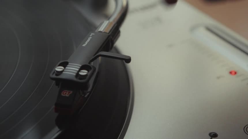 A hand gently lowers the needle of a record player onto a spinning vinyl disc in slow motion