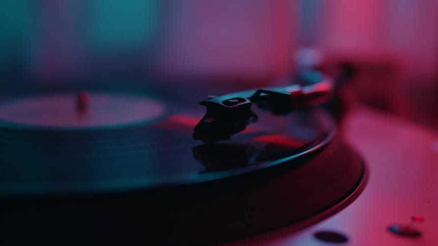A close-up shot of a spinning vinyl record on a turntable under atmospheric pink and blue neon lights