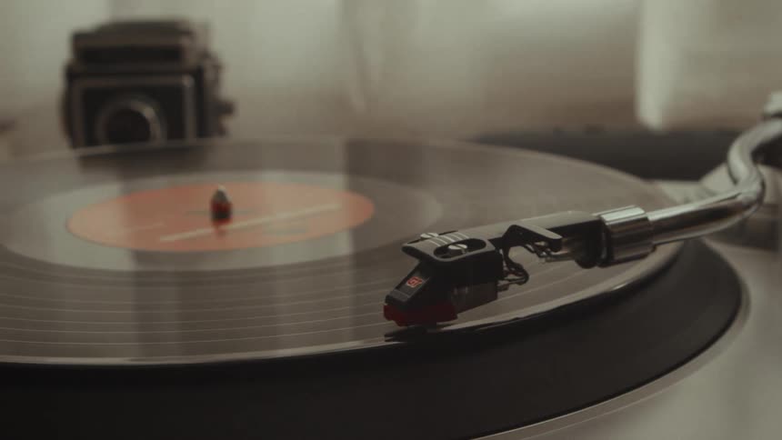 A person's hand gently places the needle onto a spinning vinyl record, starting the music on a vintage turntable