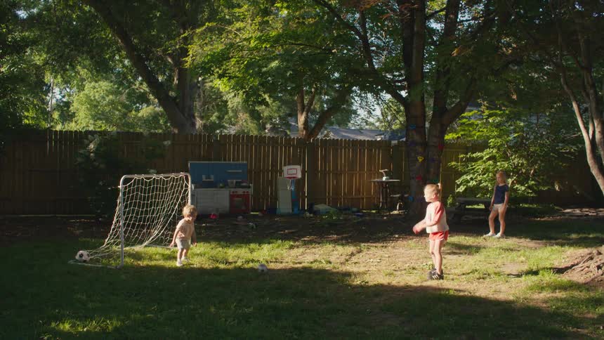 A mother and her three young children enjoy a casual game of soccer in their sun-dappled backyard