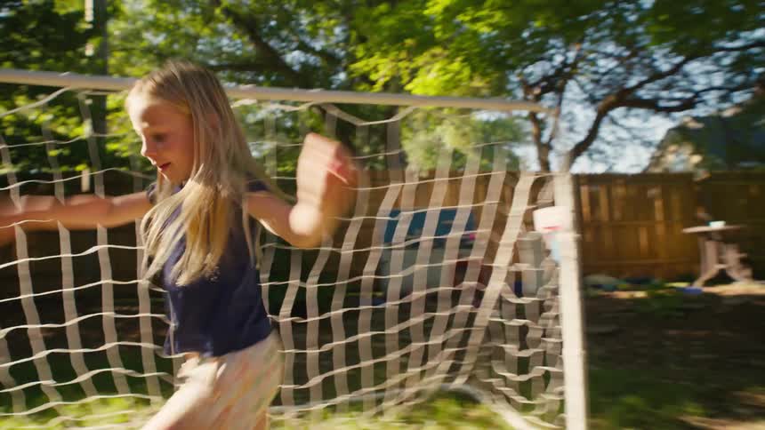 A woman scores a soccer goal against a little girl in their sunny backyard, and the two celebrate with a joyful high-five