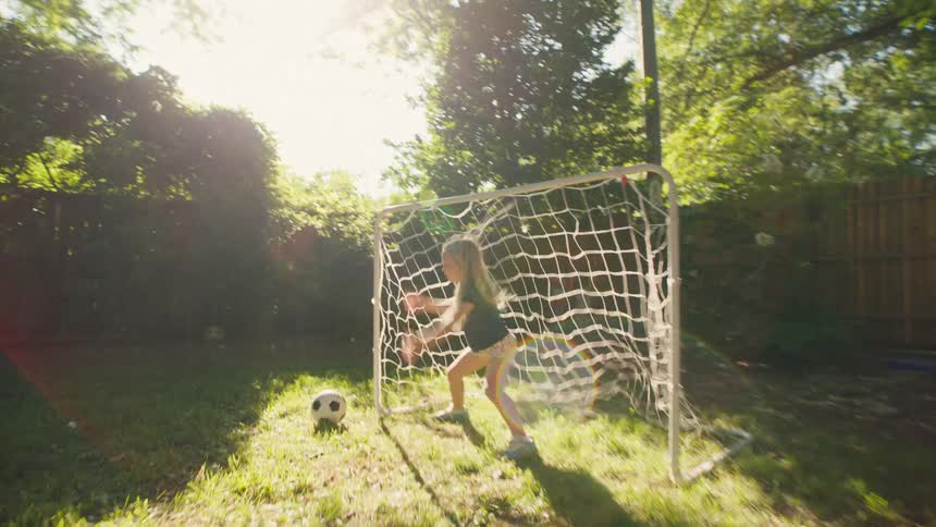 A mother and daughter enjoy a playful game of soccer in their sunny backyard, culminating in a celebratory high-five after a great save