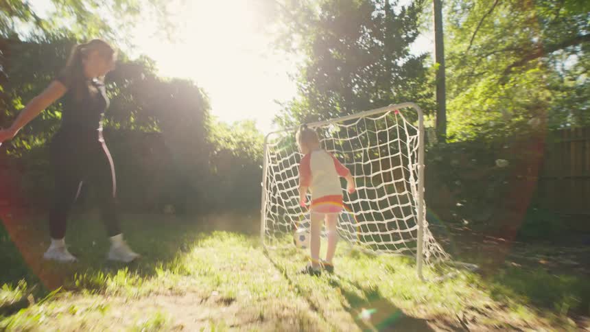 A mother and daughter play soccer in their backyard on a sunny day
