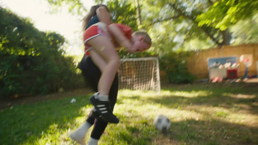 A playful mother picks up her young son and spins him around as they enjoy a game of soccer in the backyard