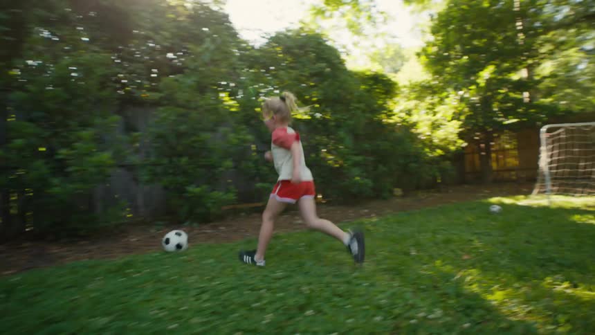 A happy mother and her two young daughters play soccer together in their backyard on a sunny day
