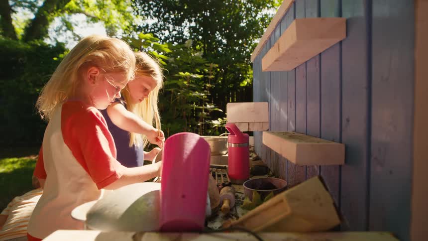 Three young siblings play together in their outdoor mud kitchen on a sunny day in the backyard