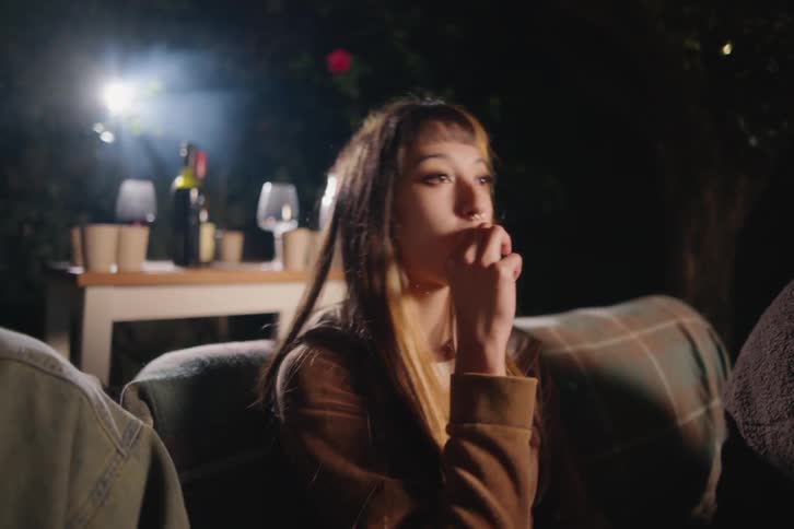 A captivated young woman watches a movie projected in her backyard during a cozy outdoor gathering at night