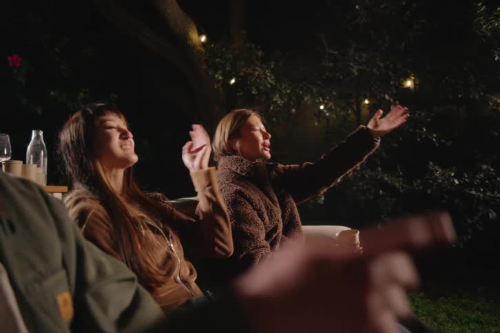 A group of friends enjoys a cozy movie night in the backyard, eating popcorn and reacting to the film