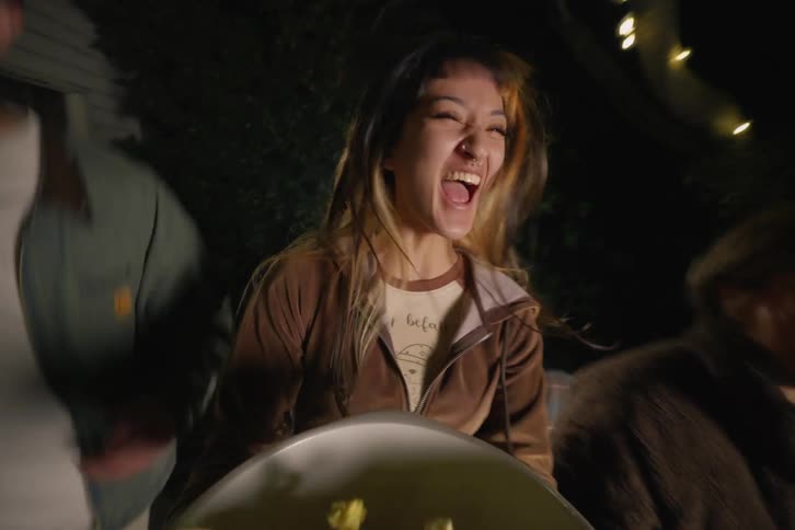 Excited friends jump for joy and spill popcorn while watching something thrilling outdoors at night