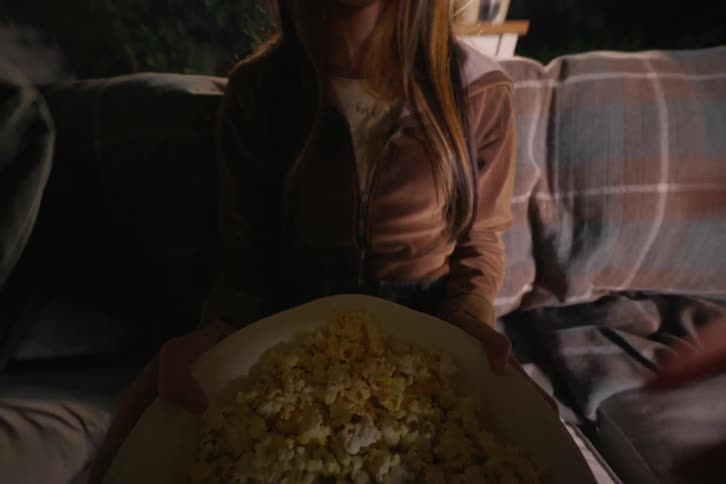 A first-person view of bringing a large bowl of fresh popcorn to friends for a cozy outdoor movie night
