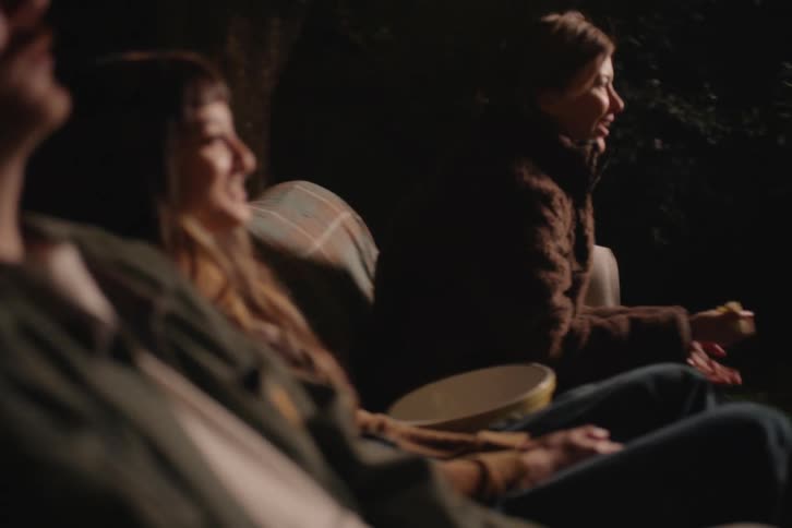 Excited friends cheer and react enthusiastically while watching an outdoor movie in the backyard at night