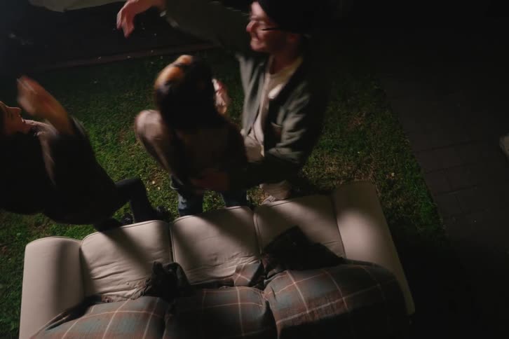 A group of friends spontaneously jump up from their outdoor couch and start dancing and celebrating while watching a movie in their backyard at night