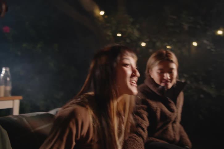 Happy friends laugh and enjoy snacks during an outdoor movie night in the backyard with a projector