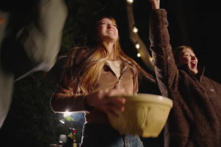 A group of excited friends jump up from their couch and cheer wildly while watching a movie on a projector outdoors at night
