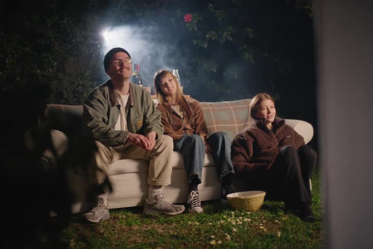 A group of young friends have a cozy backyard movie night, cheering excitedly at the screen