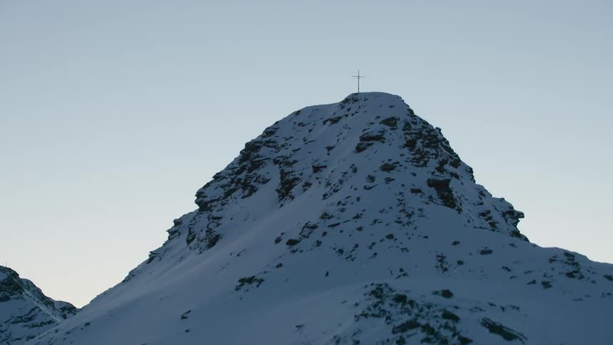 A large cross stands on a snow covered mountain peak