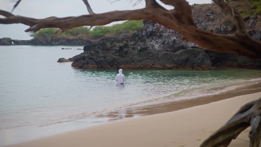 A lone fisherman casts their line into the tranquil waters of a secluded sandy beach cove