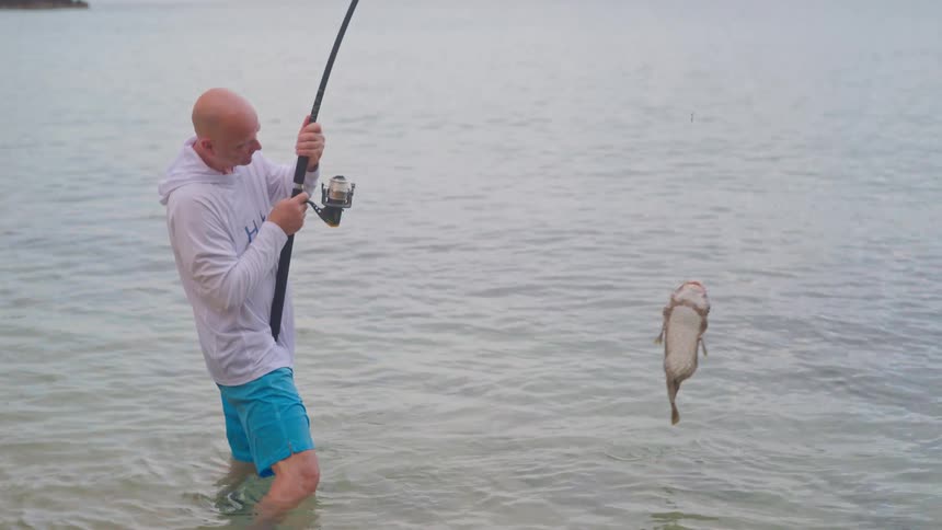 A fisherman proudly reels in a large, jumping pufferfish from the ocean in super slow motion