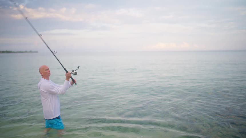 A fisherman casts his line into the calm ocean water during a peaceful morning