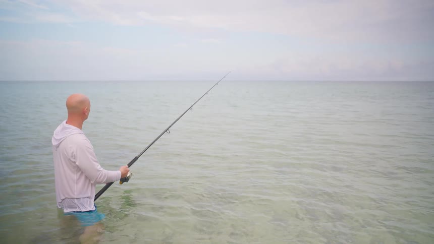 A fisherman patiently waits for a bite while standing waist-deep in the calm, clear ocean