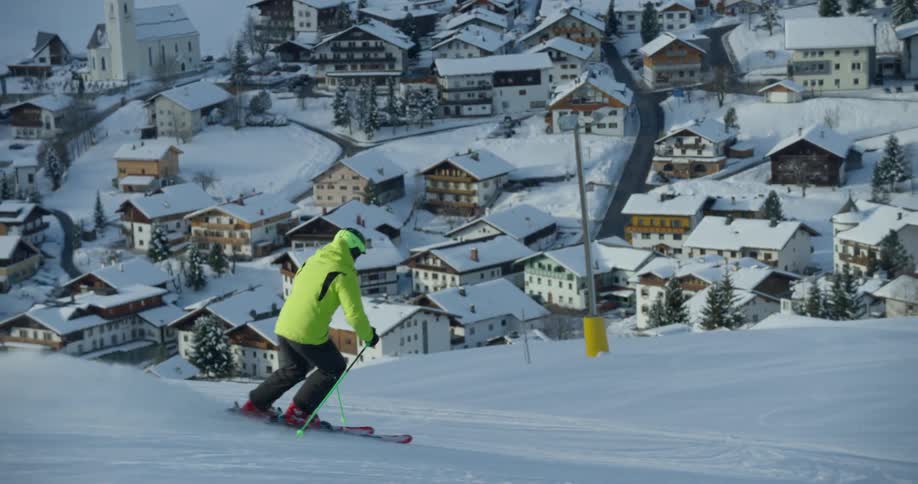 A man in a yellow coat is skiing