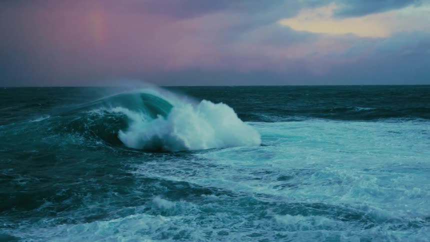 A powerful, turquoise ocean wave crashes in dramatic slow motion under a stormy purple sky with a faint rainbow on the horizon