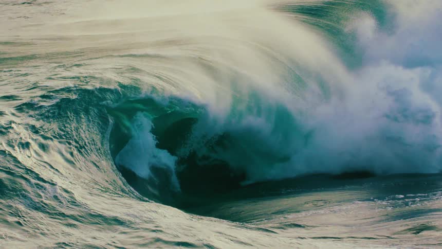 A powerful, emerald green ocean wave curls into a barrel and breaks in dramatic slow motion, showcasing the raw force of nature