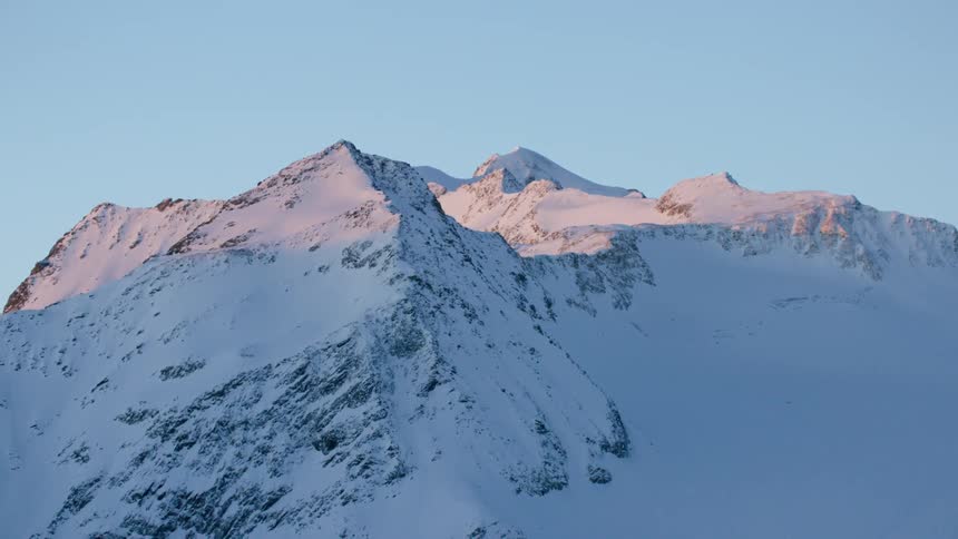The sun touches the tops of a snow-covered mountain range at dawn