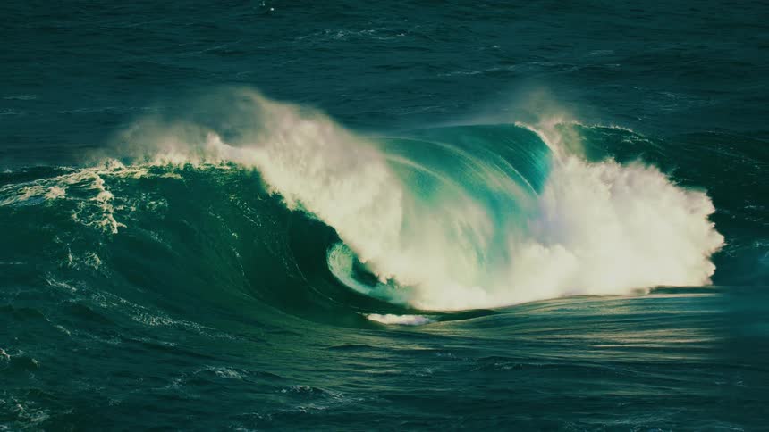 An epic, dark green ocean wave curls and crashes in dramatic slow motion