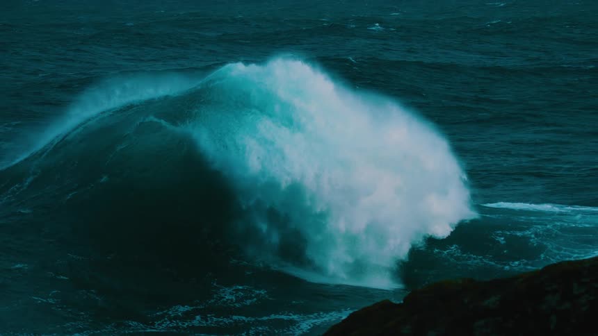 A powerful turquoise ocean wave curls and crashes in dramatic slow motion