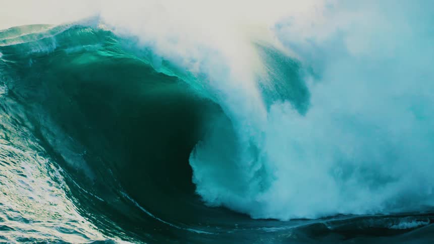 A massive, powerful turquoise ocean wave barrels and crashes in mesmerizing slow motion