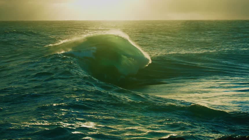 A huge, beautiful wave rolls through the sunlit ocean and breaks in spectacular slow motion