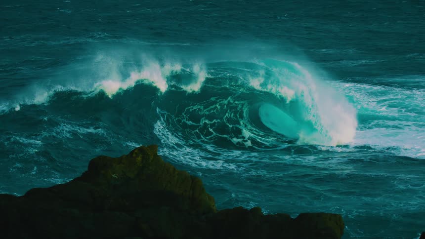 A stunning and massive turquoise wave curls and breaks in the deep ocean in dramatic slow motion