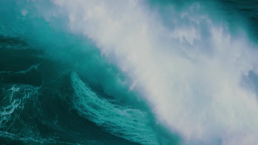 A massive teal-colored ocean wave curls into a barrel before crashing in dramatic slow motion