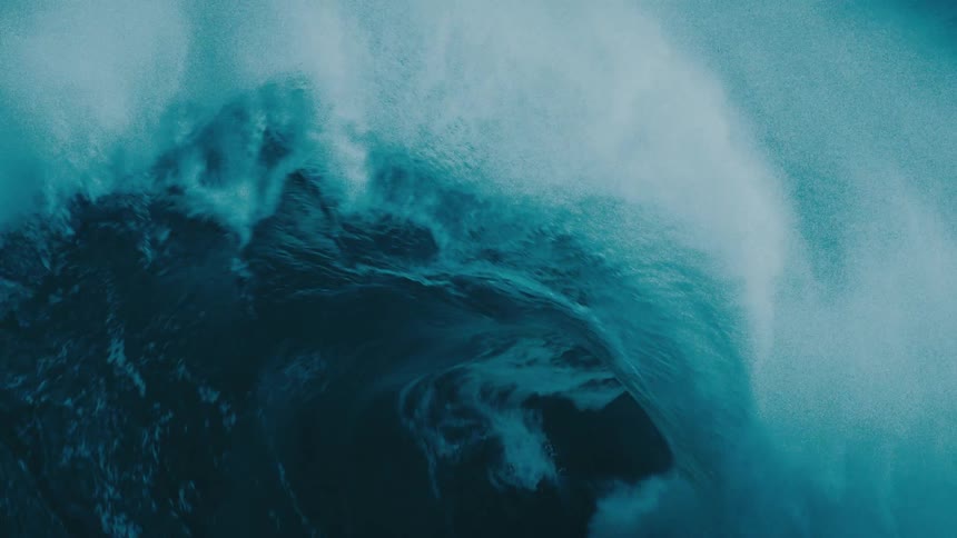 An epic close-up of a massive, dark blue ocean wave building and crashing in dramatic slow motion