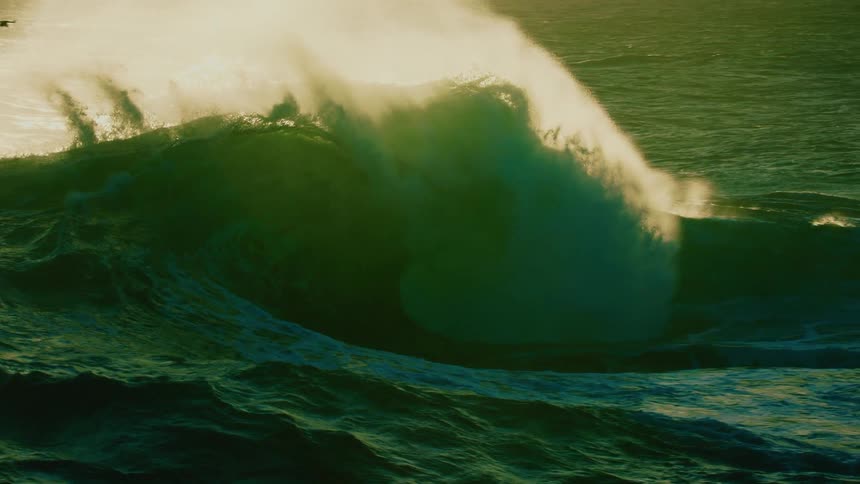 A massive ocean wave illuminated by golden light builds and crashes in dramatic slow motion