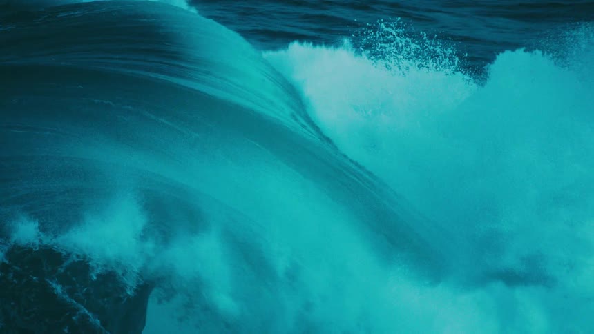 A breathtaking slow-motion shot captures the immense power and beauty of a massive turquoise ocean wave as it curls and breaks