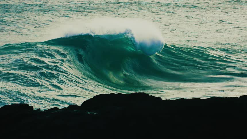 A massive turquoise ocean wave curls into a perfect barrel before crashing with explosive force in dramatic slow motion