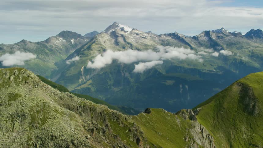 Clouds around green and rocky mountain peaks
