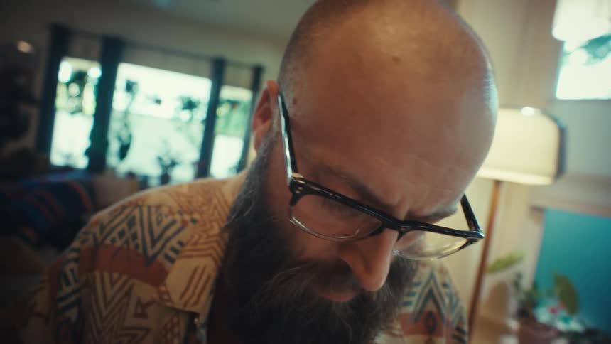 Close up of a focused, bearded man with glasses writing creative notes in a journal at home