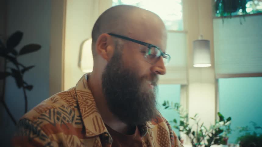 Slow zoom close-up profile of a focused bearded man with glasses working in a naturally lit room