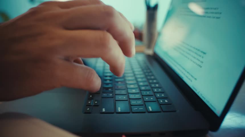 A stylized close-up dolly shot of hands typing on a laptop keyboard in a workspace