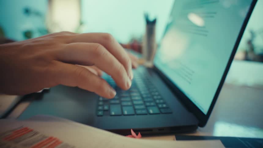 A cinematic close-up shot pulls focus from hands typing on a laptop to handwritten work notes on a desk