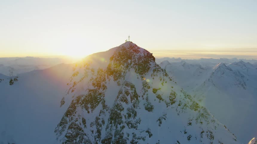 A large cross stands on a snow covered mountain peak
