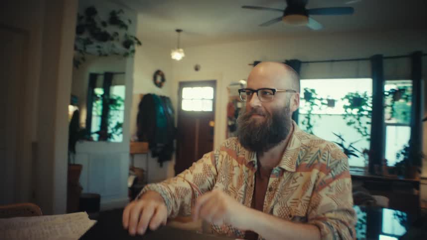 A bearded man with glasses working from home on his laptop smiles with satisfaction as he closes it, finishing his work for the day