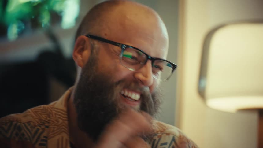 Close-up shot of a joyful bearded man with glasses rubbing his hands together in excitement and laughing