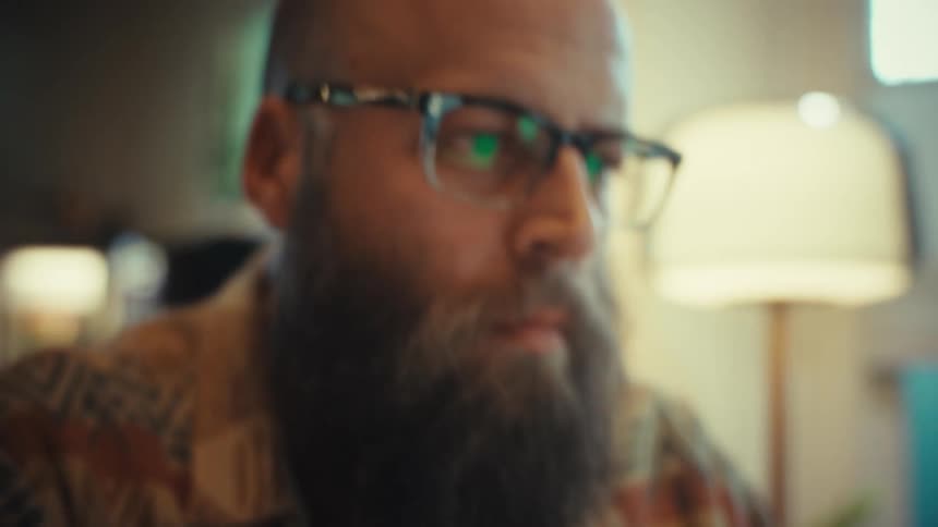 Close-up of a bearded man's hands typing on a laptop, with a focus pull to his concentrated face as he works