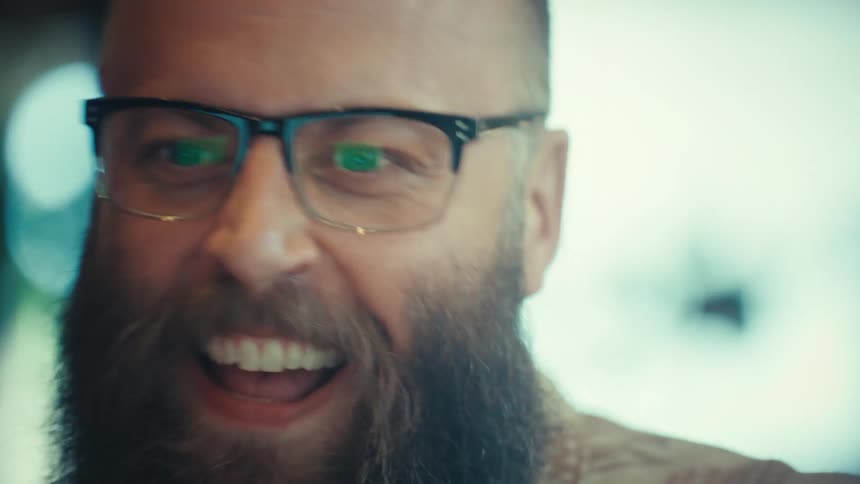 An ecstatic bearded man in glasses shouts with joy and celebrates a success while working on his computer